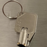 Rectangular metal key with number 1004 on key ring, on a smooth metallic surface.