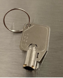 Rectangular metal key with number 1004 on key ring, on a smooth metallic surface.