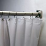 Stainless steel rod with white shower curtain and metal rings on wall.