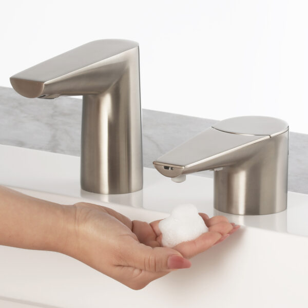 Person using stainless steel soap dispenser over sink, foam dispensed onto hand.