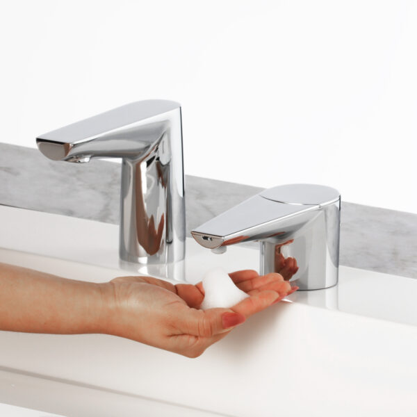 Person using a chrome soap dispenser on a white countertop next to a matching faucet.