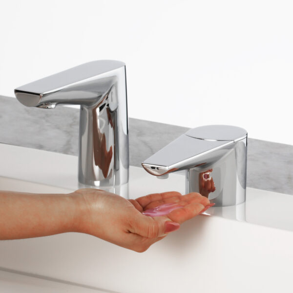 Hand below chrome soap dispenser with pink soap, beside a matching faucet.