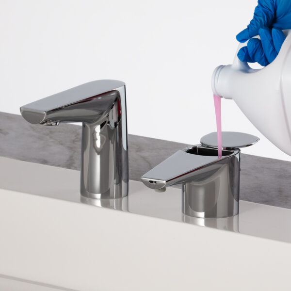 Person with blue gloves pours pink liquid into chrome dispenser by faucet.