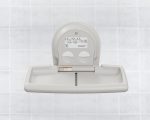 Wall-mounted baby changing station with open platform and instructions, against tiled background.