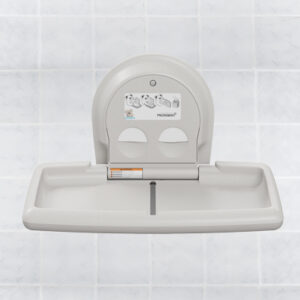 Wall-mounted baby changing station with open platform and instructions, against tiled background.