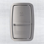 Stainless steel wall-mounted paper towel dispenser against tiled background.