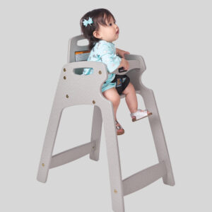 Toddler in light blue outfit seated in gray high chair with safety strap and blue hair bow.